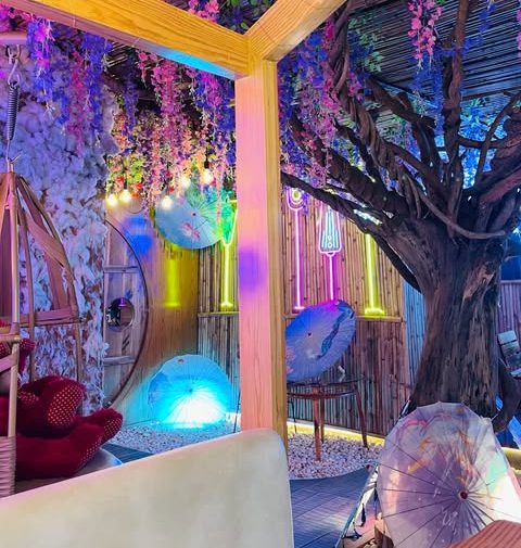 Wooden cabin seating under purple wisteria with paper umbrellas at The Cafe Bolt